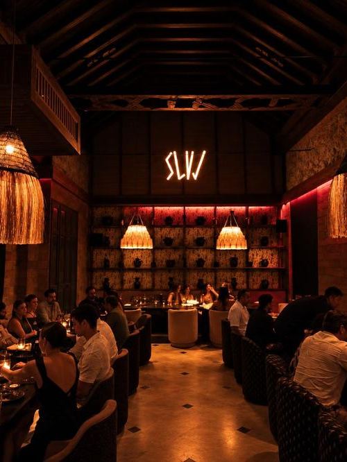 The SLVJ neon sign over the back bar, with pendant lamps and guests at dinner.